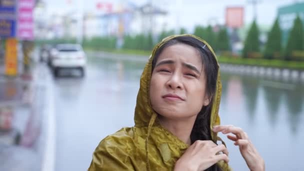 Asijské dívka nosí žlutý plášť v deštivý den stojící na silnici, období dešťů počasí klima lije déšť, smůlu dostat mokré, zatímco jde ven do práce, auto a motocykl procházející - Záběry, video