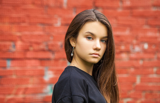Portrait of a young teenage girl on a red brick wall background - Zdjęcie, obraz