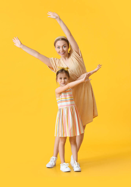 Dancing young woman and her little daughter on color background - Photo, Image