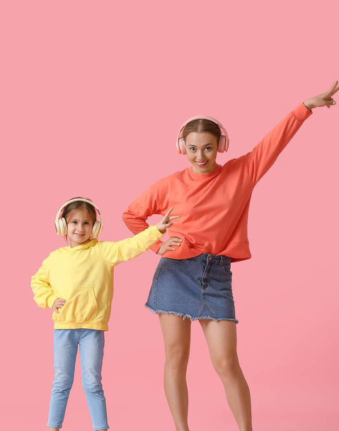 Young woman and her little daughter dancing and listening to music on color background - Foto, afbeelding