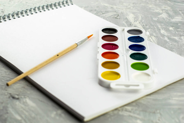 Aquarellfarben Pinsel und Skizzenbuch zum Zeichnen auf einer grau-weißen Oberfläche. Hochwertiges Foto - Foto, Bild