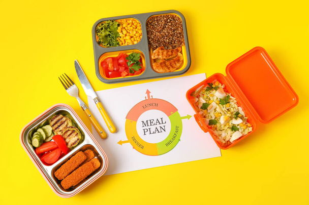Containers with food, cutlery and paper with text MEAL PLAN on yellow background - Photo, Image