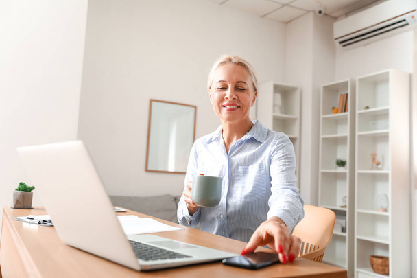 Mujer madura bebiendo café mientras trabaja en la oficina - Foto, Imagen