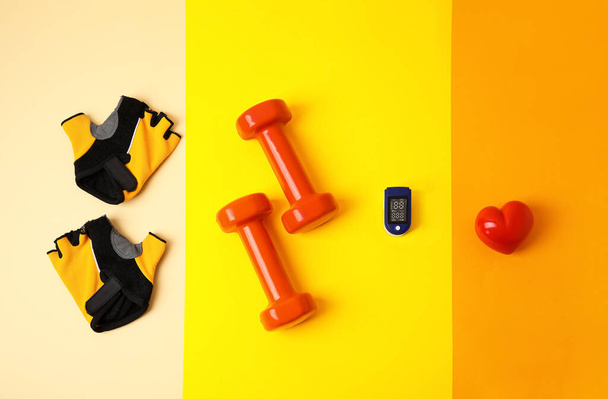 Oxímetro de pulso, mancuernas, guantes de bicicleta y corazón sobre fondo de color - Foto, Imagen