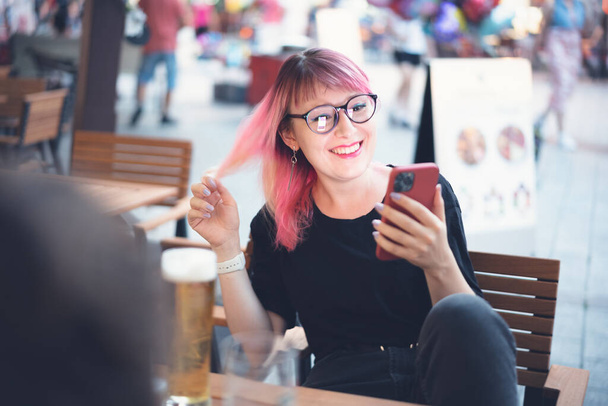 Young happy european woman 30 years old hipster with pink hair with a smartphone in her hands in a street cafe - Zdjęcie, obraz