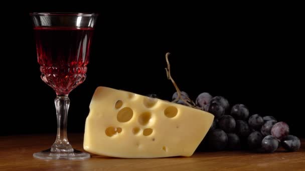 Stuk kaas, glas met wijn en druiven op een zwarte achtergrond - Video