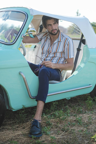 retrato de belo homem modelo italiano de cabelos escuros com olhos claros com barba em um carro tiffany italiano velho. Foto de alta qualidade - Foto, Imagem
