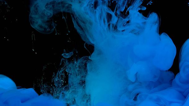 Blue watercolor ink in water on a black background. Waves and drops of blue paint. Blue cloud of ink. Cosmic magic background. Beautiful abstract background. - Фото, изображение