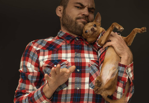 再生されたシャツと彼の膝の犬の大人の男の肖像画。不快な感情、傲慢、停止ジェスチャーの表現、楽しいミーム. - 写真・画像