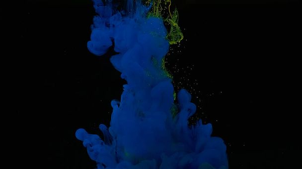 Blue and yellow watercolor ink in water on a black background. Blue-yellow cloud of ink. Cosmic magic background. Waves and drops of blue-yellow colors. Beautiful abstract background. - Photo, Image