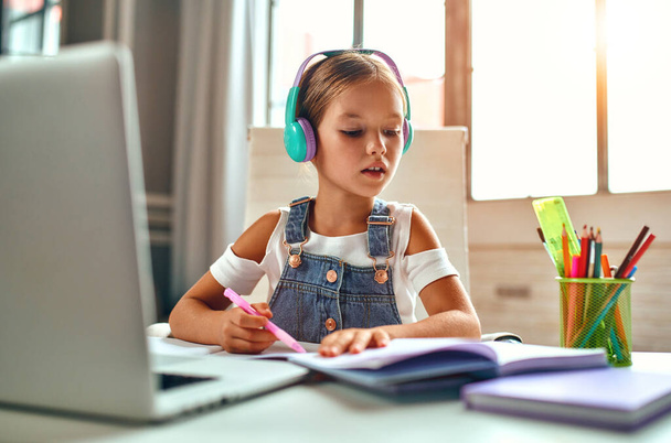 Trening online. Dziecko w słuchawkach słucha lekcji na laptopie. Szkoła w domu w czasie pandemii i kwarantanny. - Zdjęcie, obraz