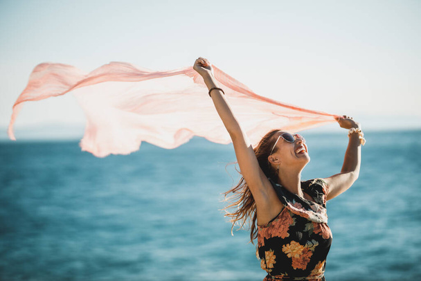Приваблива молода жінка в квітковому одязі з шарфом розважається і насолоджується літнім відпочинком на пляжі
. - Фото, зображення