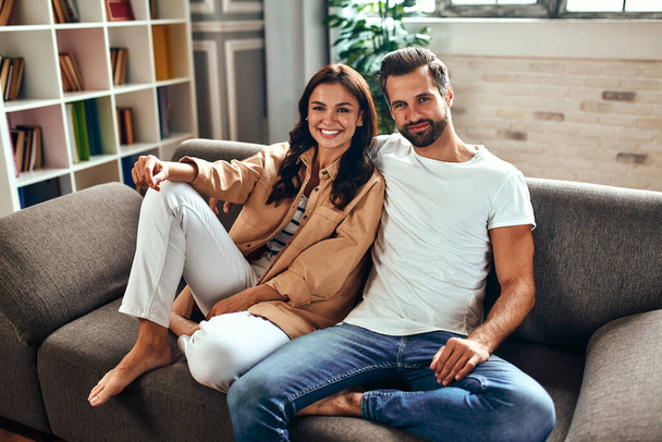 Les jeunes couples amoureux sont assis sur le canapé à la maison. Un couple marié se relaxe dans le salon. - Photo, image