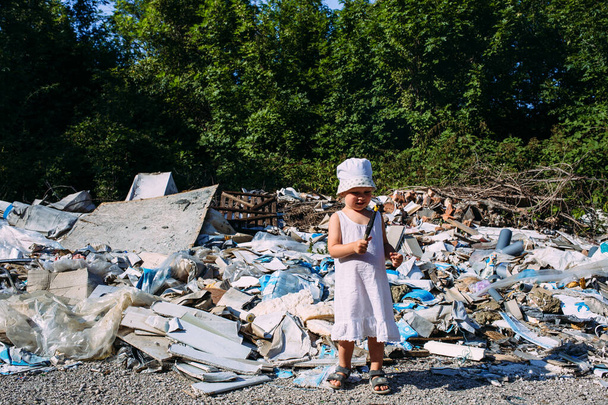 Little girl at a dump among a heap of scattered garbage in the forest.  - Photo, Image