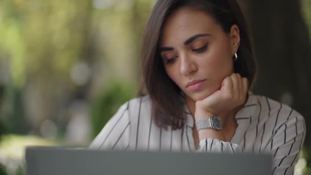 Pensive woman Brunette arabic Hispanic ethnic group sits at a table in a summer cafe with a laptop. Serious business woman pondering problem solving and business development strategy - Footage, Video
