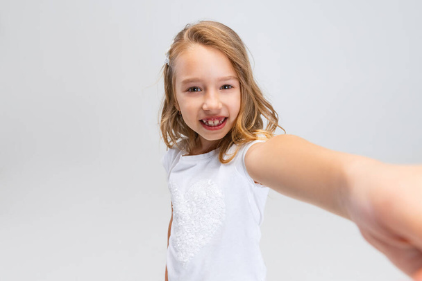 Close-up beautiful little smiling girl with long hair in modern stylish outfit looking at camera isolated on white studio background. Happy childhood concept. - 写真・画像