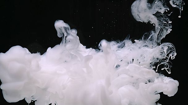 White watercolor ink in water on a black background. Waves of milky ink and splashes of white paints in the water. Beautiful abstract background. - Foto, Imagen