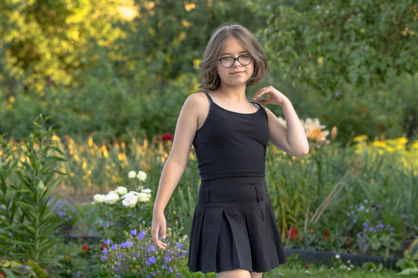Girl in glasses in black clothes posing in a blooming summer garden - Fotoğraf, Görsel