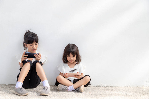 Concept kinderen en gadgets. Twee kleine meisjes broers en zussen kijken naar de telefoon en glimlachen. Ze hebben een smartphone, bekijken video 's, leren, spelen spelletjes, spreken online. Internet voor kinderen. Ouderlijk toezicht - Foto, afbeelding