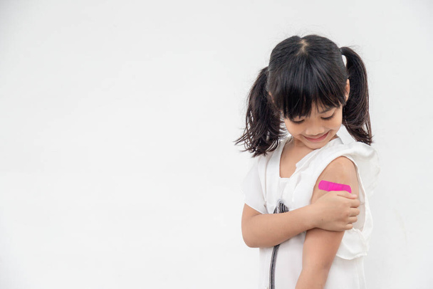 Ázsiai kislány mutatja a karját, miután beoltották vagy beoltották, gyermek immunizálás, kovid delta vakcina koncepció - Fotó, kép