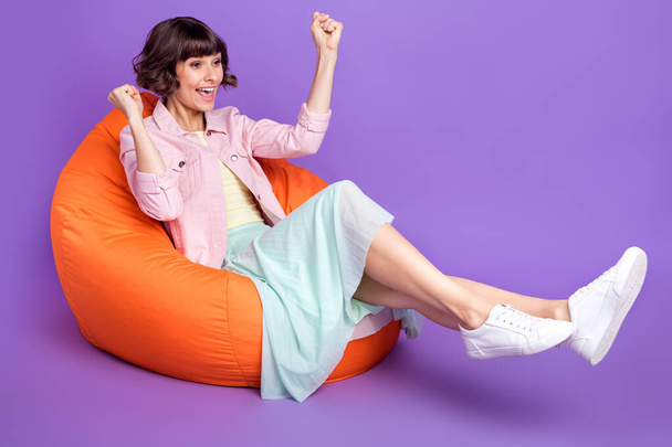 Full size photo of happy cheerful young woman look empty space sit bean bag winner isolated on purple color background - Fotoğraf, Görsel
