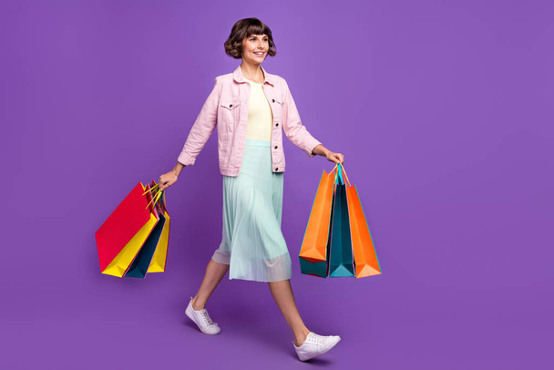 Full body photo of happy young woman walk hold hands bags sale shop isolated on violet color background - Fotografie, Obrázek