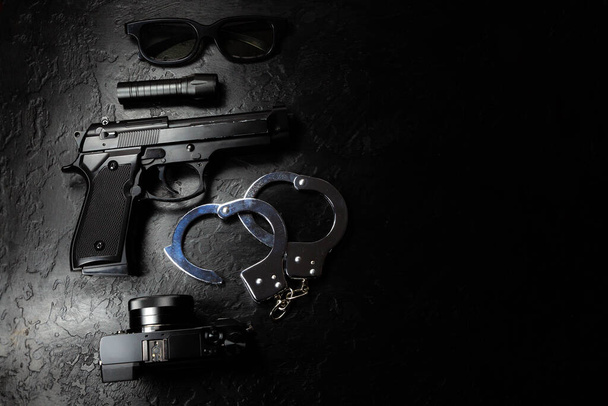 Чорна гармата, ліхтарик, окуляри, камера та поліцейський метал справжні наручники лежать на чорному тлі. Приватний детектив працює. Пошук інформації. Злочинність і пограбування, концепція в'язниці
. - Фото, зображення