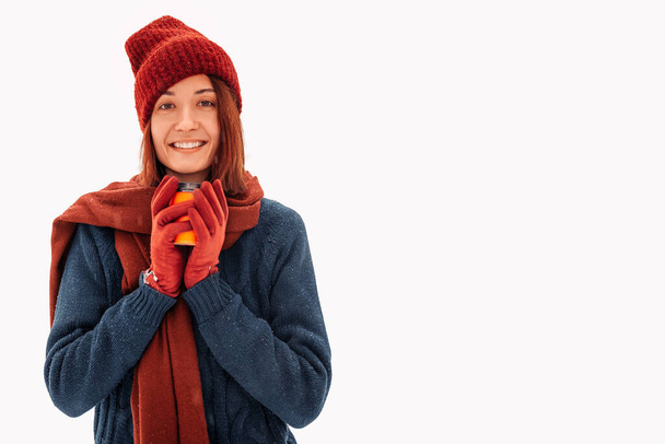 Young smiling woman in winter clothes holding a cup of coffee and looking at the camera, on a white background - Photo, Image