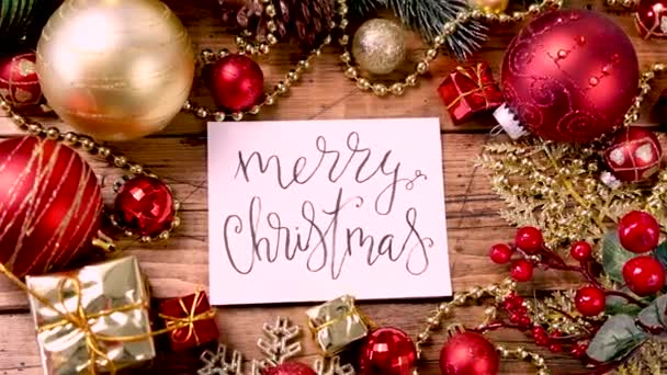 Μια κάρτα με χειρόγραφο κείμενο Καλά Χριστούγεννα με διακοσμήσεις γύρω από το ξύλινο τραπέζι πάνω όψη Zoom in - Πλάνα, βίντεο