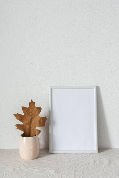 Home decor mocap, lege fotolijst bij wit geschilderde betonnen muur, takken met droge bladeren - Foto, afbeelding