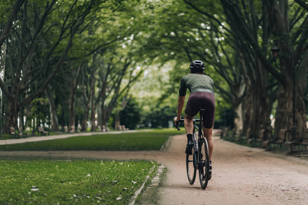 Back view of muscular cyclist in sport clothes and safety helmet biking alone on fresh air. Concept of people, outdoors activity and healthy lifestyles. - Фото, зображення