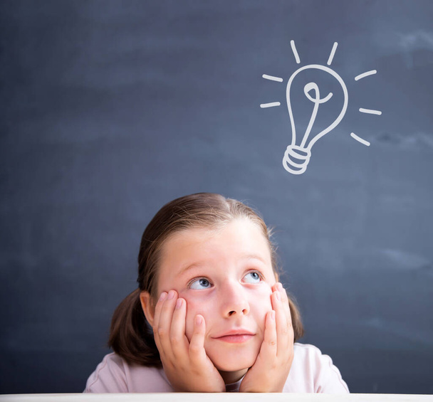 Schoolgirl in front of a blackboard with a bright idea light bulb above her head. Concept for innovation, imagination and inspirational ideas. - Photo, Image