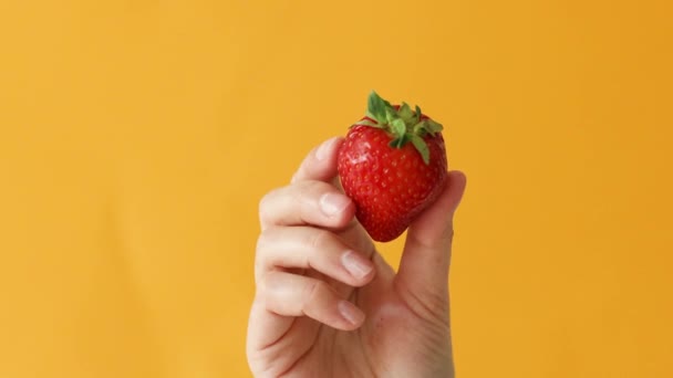 Großaufnahme einer Bio-Erdbeere in Frauenhand vor gelbem Hintergrund. Gesunde Ernährung und Lebensstil-Konzept - Filmmaterial, Video