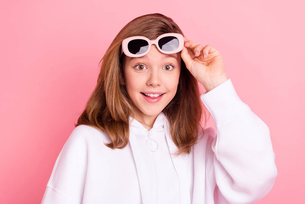 Portrait of attractive amazed cheerful girl touching specs isolated over pink pastel color background - Foto, Imagen