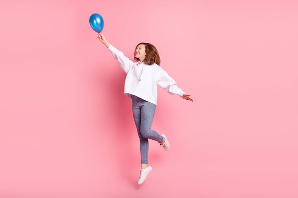 Вид в полный рост на привлекательную трехлетнюю жизнерадостную девочку, прыгающую, держа в руках воздушный шар, изолированный на розовом фоне - Фото, изображение
