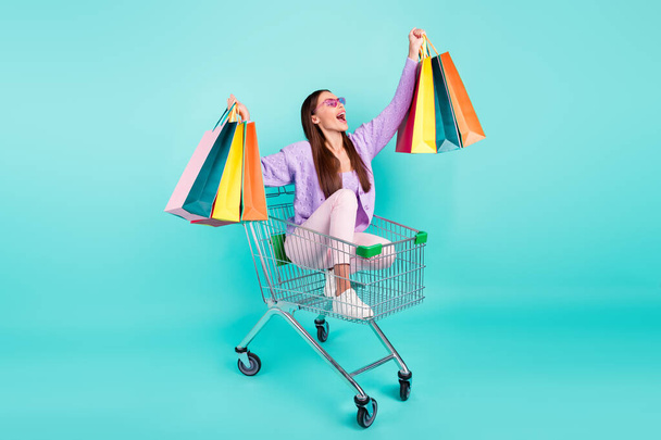 Photo of funky pretty woman dressed purple clothes dark eyewear holding bags riding shopping tray isolated teal color background - Φωτογραφία, εικόνα