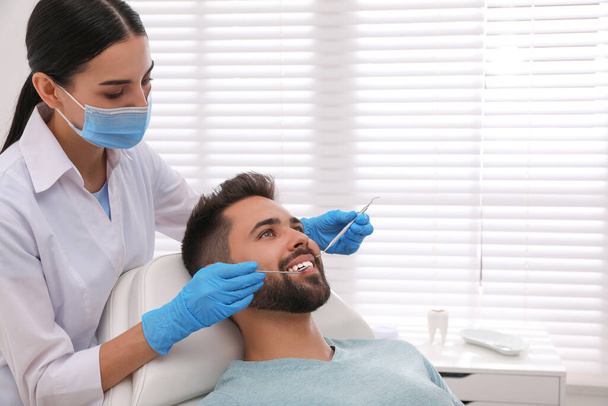 Dentist examining young man's teeth in modern clinic - 写真・画像