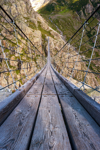 Ξύλινη κρεμαστή στενή γέφυρα καλωδίων στις Ελβετικές Άλπεις. Στη γέφυρα Τριφτ. Καλοκαίρι, μέρα, χωρίς ανθρώπους. - Φωτογραφία, εικόνα