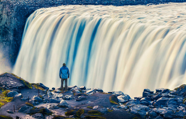 Tourist admiring view of falling water of the most powerful waterfall in Europe - Dettifoss. Jokulsargljufur National Park, Iceland. White nights view. Artistic style post processed photo. - Фото, изображение