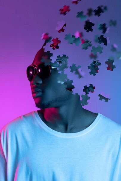 Tvůrčí koláž mladého afrického muže ve slunečních brýlích, který se dívá stranou izolovaný přes gradient fialové pozadí. Mužská hlava se skládá z dílků skládanky - Fotografie, Obrázek