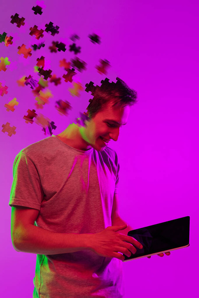 collage moderno de niño caucásico con tableta aislada sobre fondo púrpura. Cabeza masculina consiste en piezas del rompecabezas. - Foto, Imagen