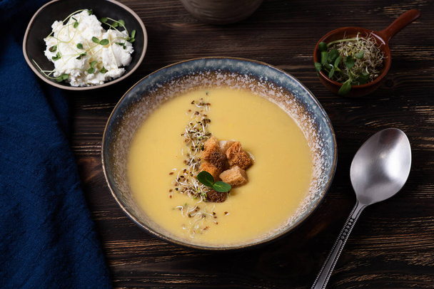 Gezonde vegetarische puree soep, bord pompoensoep met croutons, kaas en microgreens op een donkere houten ondergrond, close-up. - Foto, afbeelding