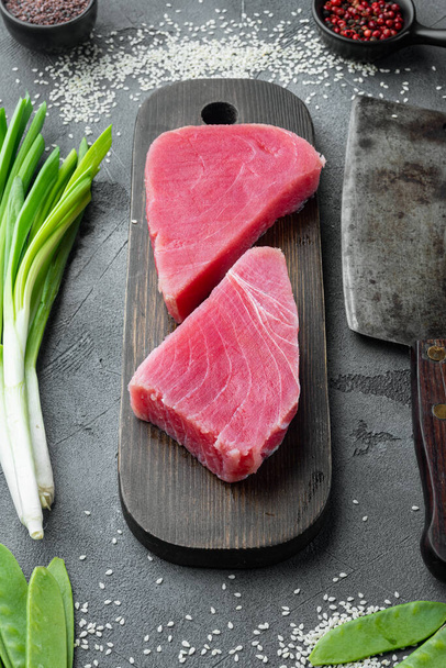 Филе тунца сырой органический стейк с ингредиентами, на деревянной разделочной доске, и старый нож мясника тесак, на сером фоне камня - Фото, изображение