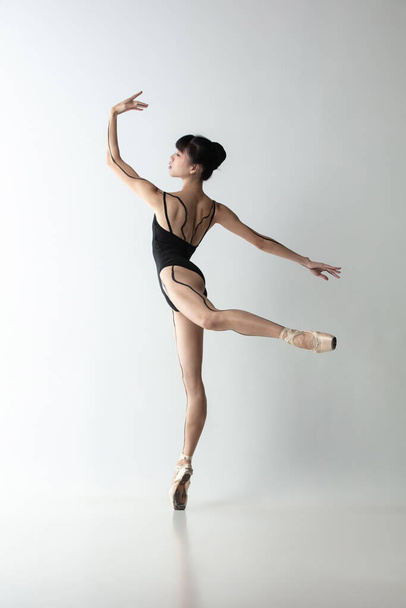 Full-length portrait of graceful ballet dancer, ballerina dancing isolated on light gray studio background. Art, motion, action, flexibility, inspiration concept. - Foto, imagen