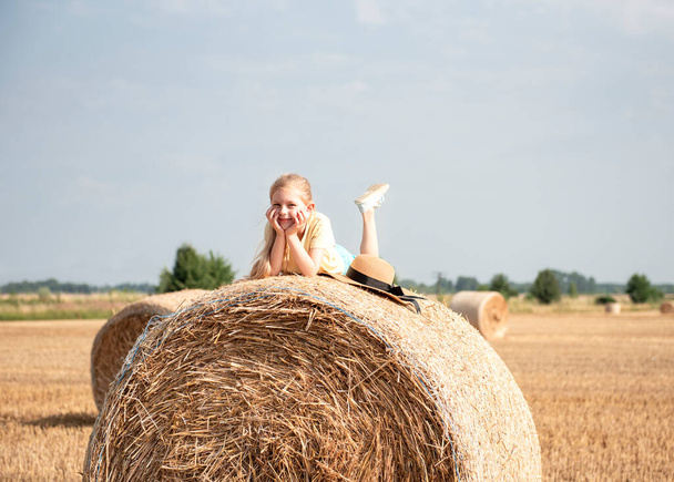 Petite fille qui s'amuse dans un champ de blé un jour d'été. Enfant jouant au champ de balles de foin pendant la récolte. - Photo, image