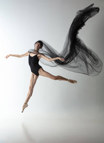 Retrato de una joven bailarina japonesa adorable bailando con tela transarente, telaraña negra aislada sobre fondo de estudio gris claro. Belleza, arte de línea, concepto de emociones. - Foto, Imagen
