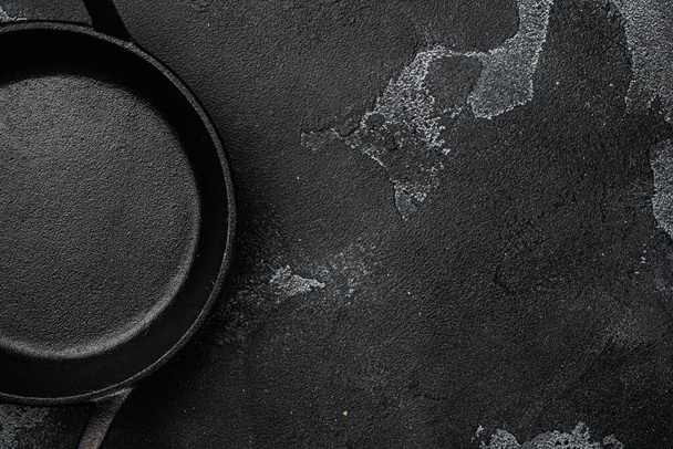 Empty cast iron skillet set with copy space for text or food with copy space for text or food, top view flat lay, on black dark stone table background - Photo, Image