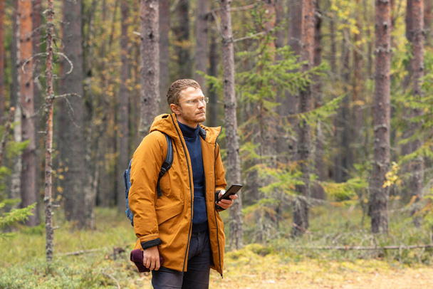 Portrait of a Caucasian man with a smartphone in his hand. A man catching a cellular network on a smartphone while walking in the forest - Foto, afbeelding