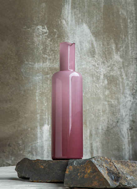 A pink glass bottle for water drinking and surface reflections on rock floor. Copy space, Selective focus. - Foto, immagini
