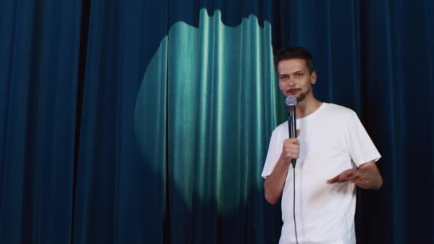 Guy in een wit T-shirt treedt op het podium op tegen een blauwe doek achtergrond - Video